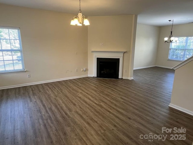unfurnished living room with a fireplace with flush hearth, dark wood-type flooring, a chandelier, and baseboards