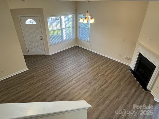 unfurnished living room featuring a fireplace, a notable chandelier, dark wood-style flooring, and baseboards