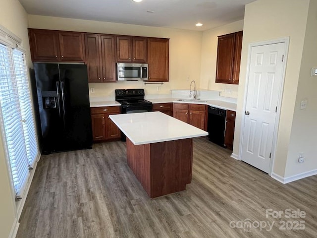 kitchen featuring a center island, black appliances, wood finished floors, and a sink
