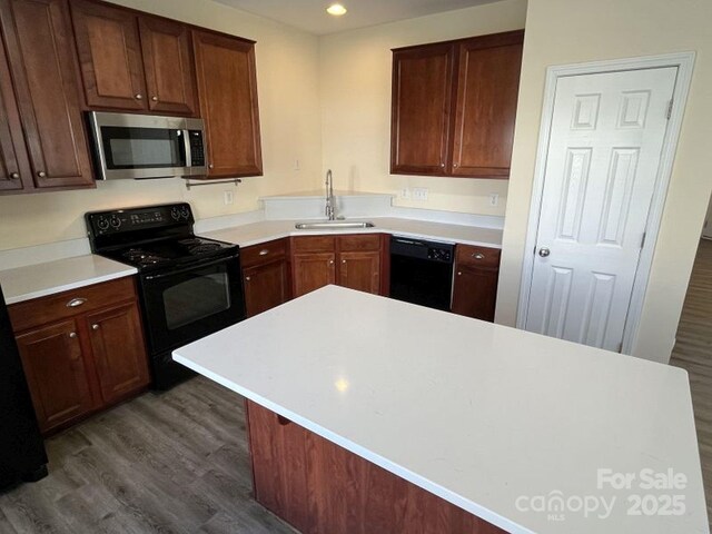 kitchen featuring recessed lighting, a sink, dark wood-type flooring, black appliances, and light countertops
