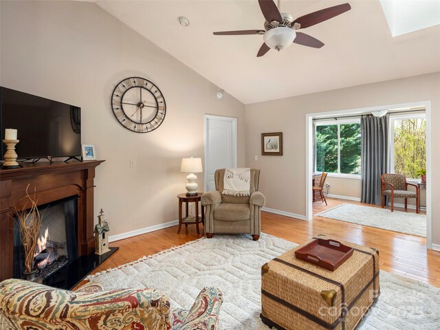 living room with baseboards, wood finished floors, a warm lit fireplace, and ceiling fan