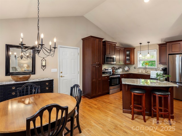 kitchen with a sink, tasteful backsplash, light wood-type flooring, lofted ceiling, and appliances with stainless steel finishes