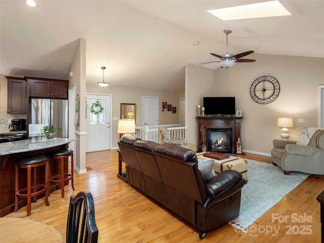 living room with vaulted ceiling with skylight, light wood finished floors, and baseboards
