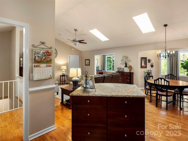 kitchen with vaulted ceiling with skylight, hanging light fixtures, open floor plan, light wood finished floors, and a kitchen island