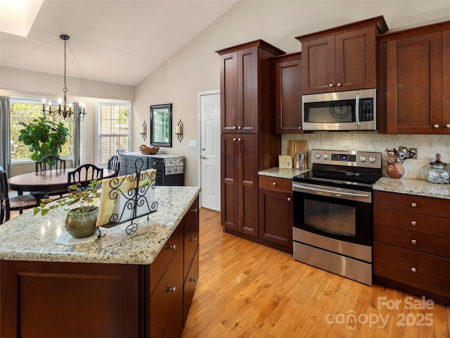 kitchen featuring tasteful backsplash, an inviting chandelier, stainless steel appliances, light wood-style flooring, and lofted ceiling