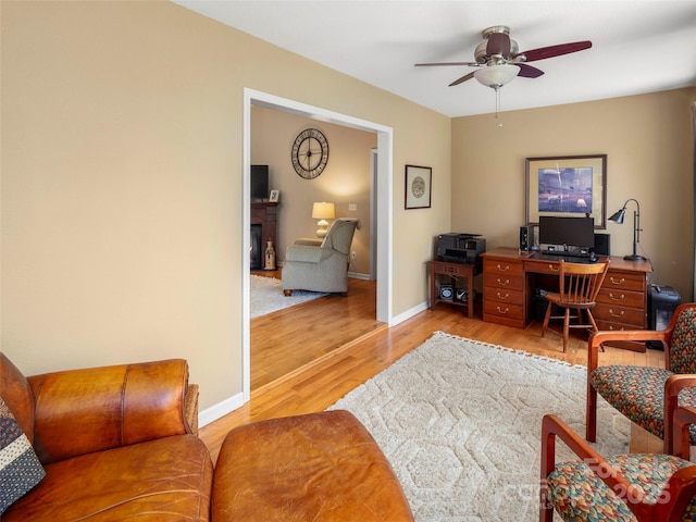 office area with light wood-type flooring, a ceiling fan, and baseboards