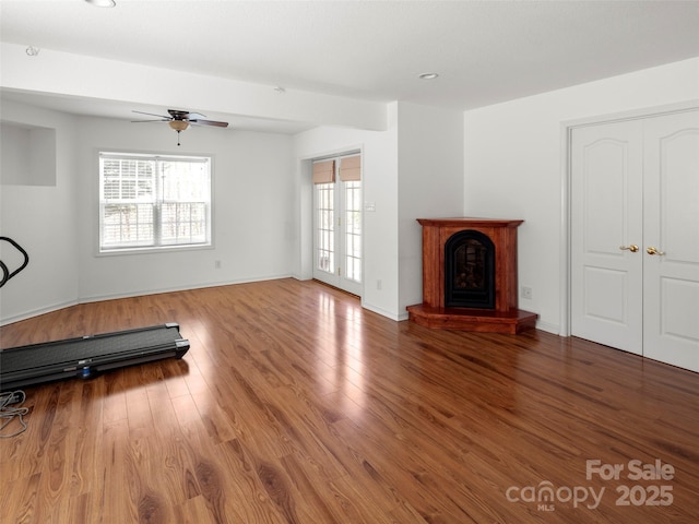 unfurnished living room featuring a ceiling fan, wood finished floors, a fireplace with raised hearth, baseboards, and recessed lighting