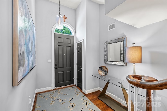 entrance foyer with wood finished floors, visible vents, a high ceiling, and baseboards