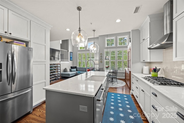 kitchen with a sink, dark wood-style flooring, stainless steel appliances, backsplash, and wall chimney range hood