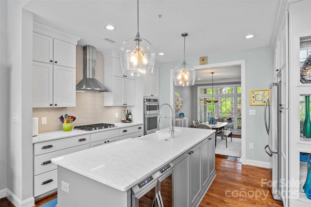 kitchen featuring wood finished floors, appliances with stainless steel finishes, wall chimney range hood, a sink, and baseboards