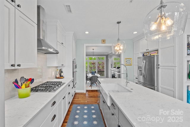 kitchen featuring an inviting chandelier, appliances with stainless steel finishes, wall chimney range hood, and a sink