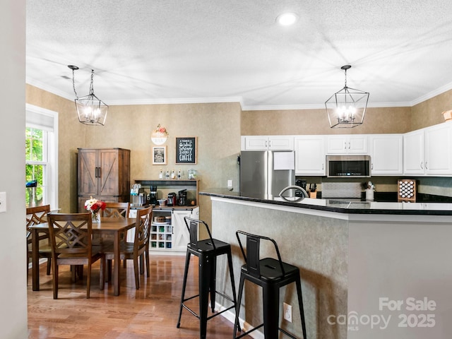 kitchen featuring white cabinets, dark countertops, stainless steel appliances, an inviting chandelier, and light wood finished floors