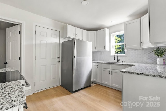 kitchen with tasteful backsplash, a sink, freestanding refrigerator, light wood finished floors, and white cabinetry