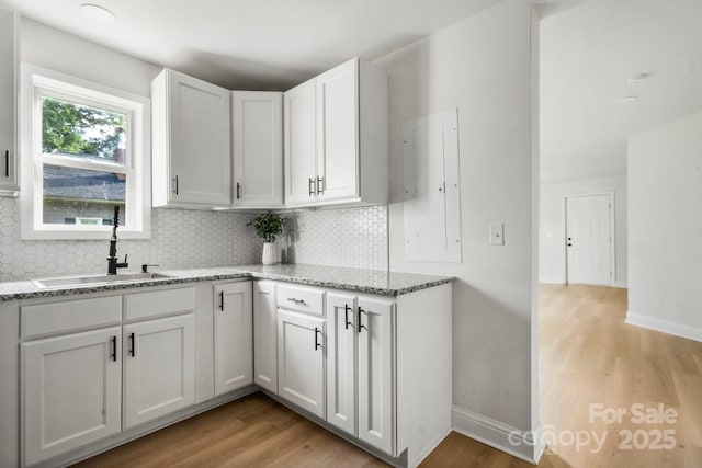 kitchen with a sink, white cabinets, tasteful backsplash, light wood-style floors, and light stone counters
