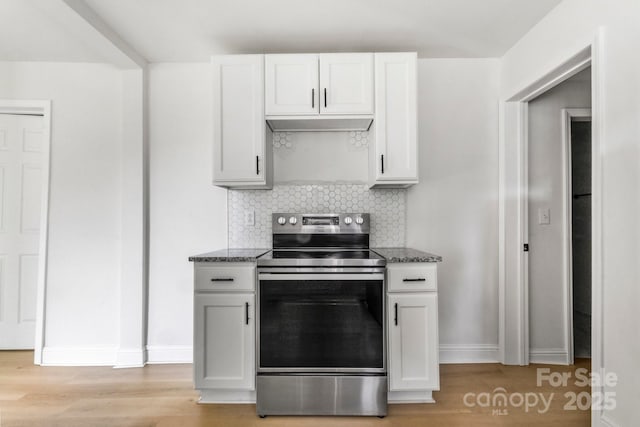kitchen featuring dark stone counters, baseboards, stainless steel electric stove, and light wood finished floors