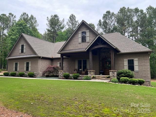 craftsman house with covered porch, a front yard, and roof with shingles