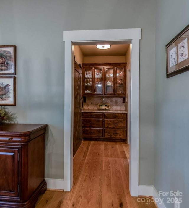bar area with light wood finished floors, baseboards, backsplash, and a barn door