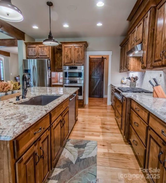 kitchen with stainless steel appliances, a sink, under cabinet range hood, a barn door, and pendant lighting
