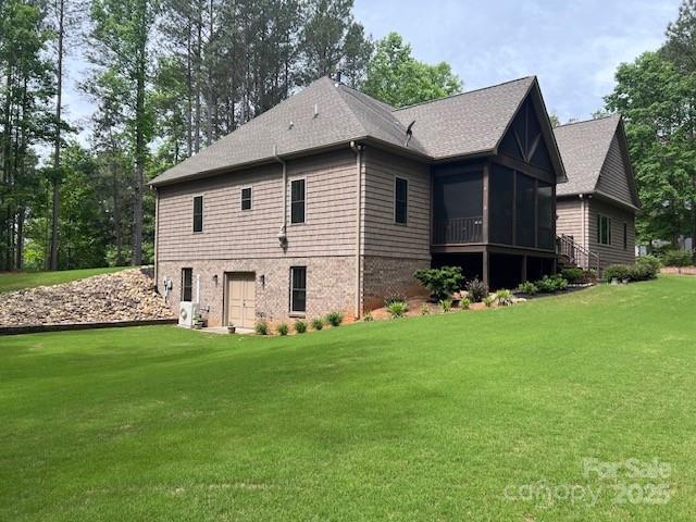 view of side of property featuring a sunroom, a lawn, and roof with shingles