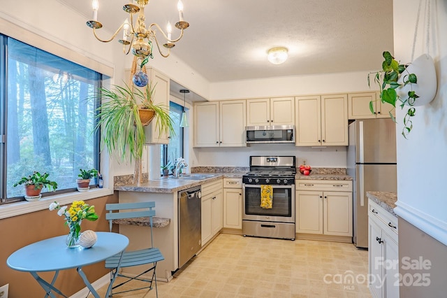 kitchen with a sink, an inviting chandelier, stainless steel appliances, and cream cabinetry