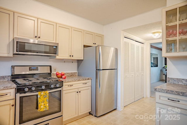 kitchen featuring light countertops, appliances with stainless steel finishes, cream cabinets, and glass insert cabinets