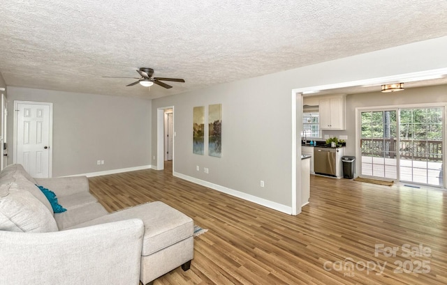 living room with light wood-type flooring, a ceiling fan, baseboards, and a textured ceiling