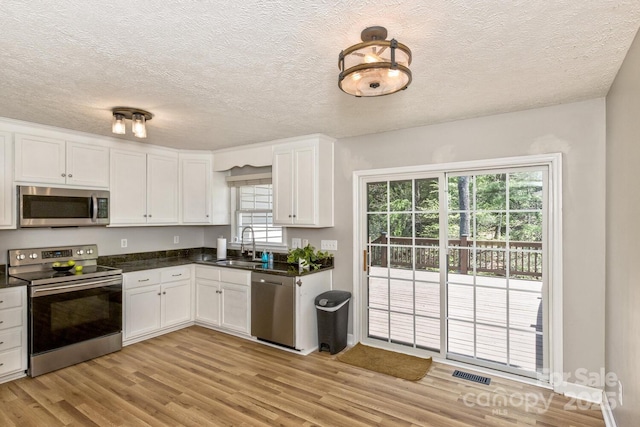 kitchen with white cabinets, dark countertops, appliances with stainless steel finishes, and a sink