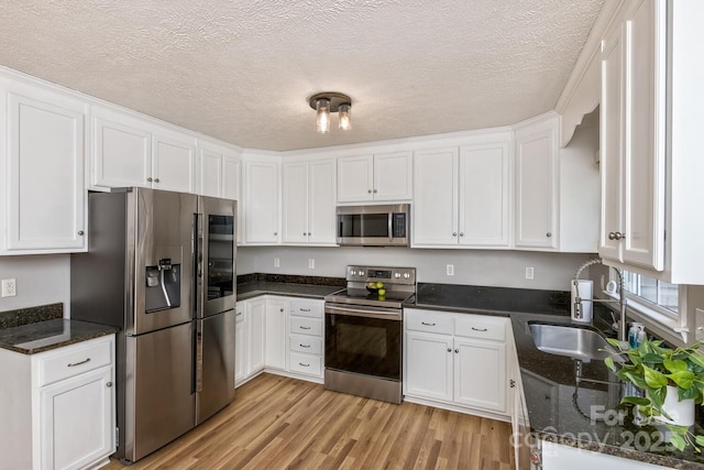 kitchen featuring white cabinets, stainless steel appliances, light wood finished floors, a sink, and a textured ceiling