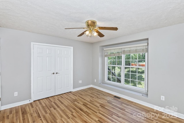 unfurnished bedroom featuring a ceiling fan, wood finished floors, a textured ceiling, a closet, and baseboards