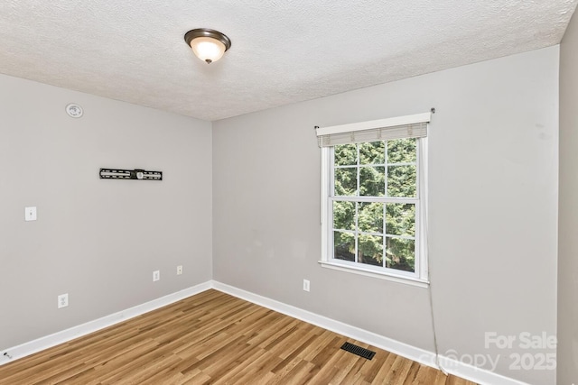 empty room featuring baseboards, light wood-style floors, visible vents, and a textured ceiling