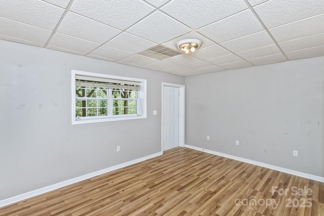 empty room featuring light wood-type flooring, a drop ceiling, and baseboards