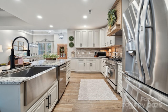 kitchen with light stone countertops, white cabinets, a sink, light wood finished floors, and stainless steel appliances