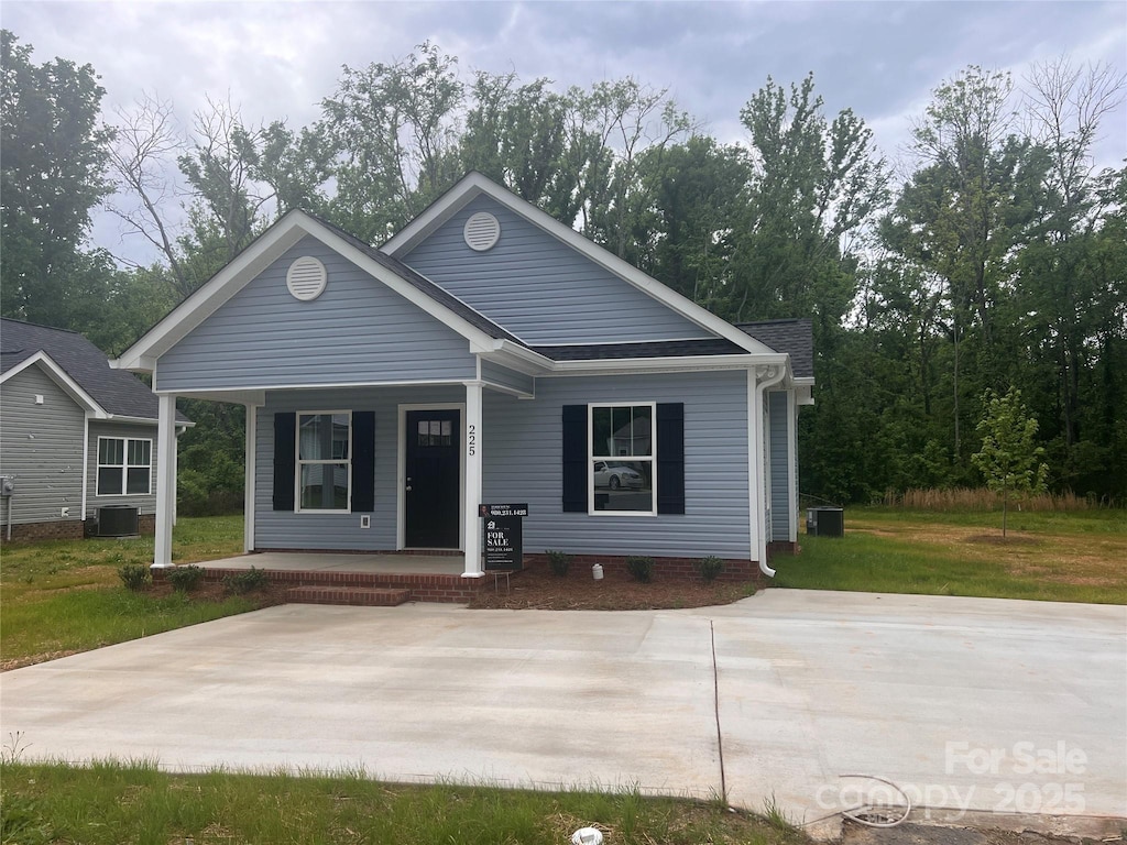 view of front of property with covered porch, a front yard, and central AC