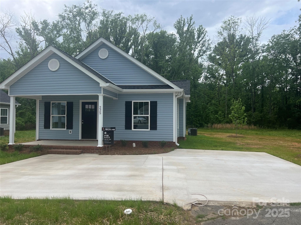 bungalow-style house with central AC unit, roof with shingles, a porch, and a front yard
