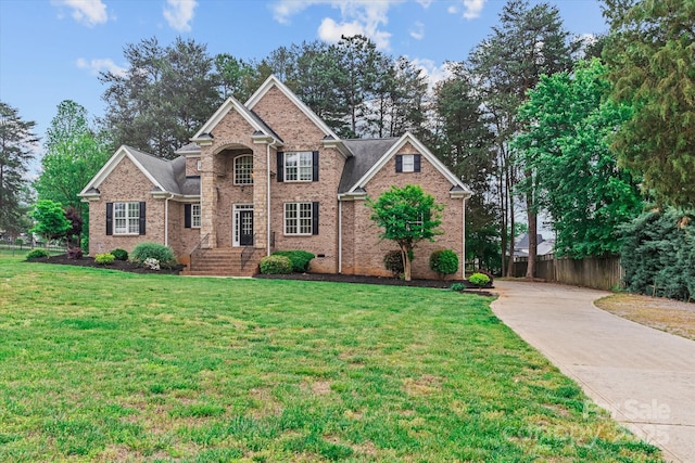 traditional-style house with driveway, fence, a front yard, and brick siding