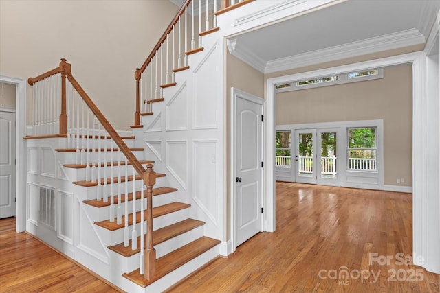 staircase with ornamental molding, french doors, wood finished floors, and a healthy amount of sunlight