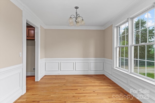 unfurnished dining area featuring wainscoting, an inviting chandelier, crown molding, and light wood finished floors