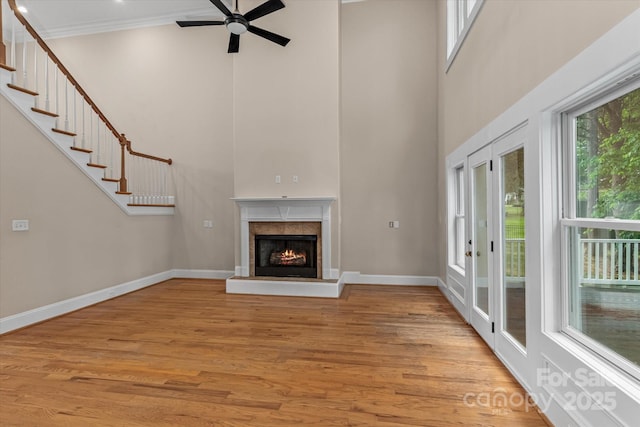unfurnished living room with crown molding, a towering ceiling, a ceiling fan, and light wood-style flooring