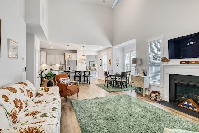 living area with light wood-style floors, a glass covered fireplace, and a high ceiling