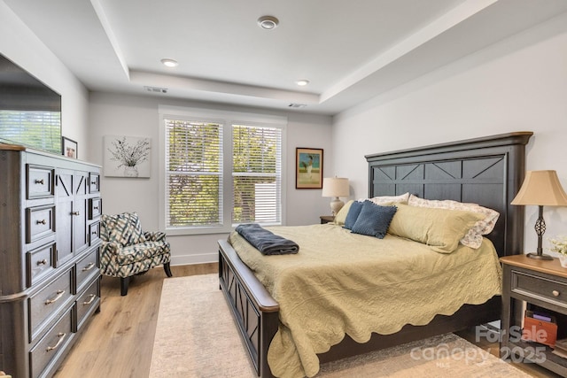 bedroom with light wood-style floors, recessed lighting, a raised ceiling, and baseboards