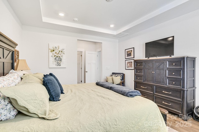 bedroom featuring recessed lighting, a tray ceiling, and wood finished floors