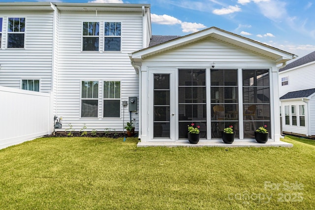 rear view of property featuring a lawn, fence, and a sunroom