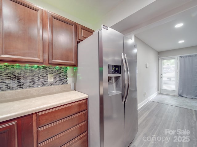 kitchen featuring decorative backsplash, light wood-type flooring, baseboards, light countertops, and stainless steel fridge with ice dispenser