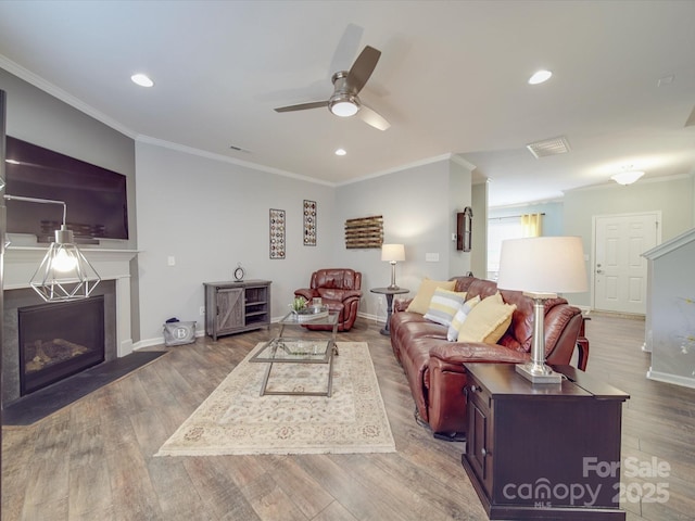 living area featuring crown molding, a fireplace with flush hearth, wood finished floors, baseboards, and a ceiling fan