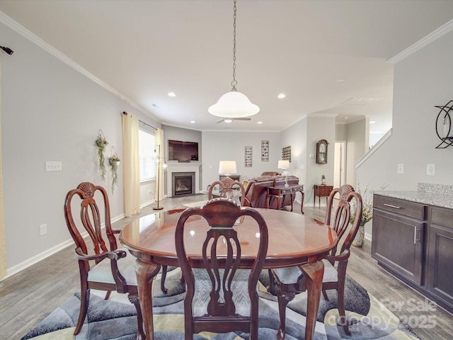 dining space featuring baseboards, recessed lighting, light wood finished floors, and a glass covered fireplace
