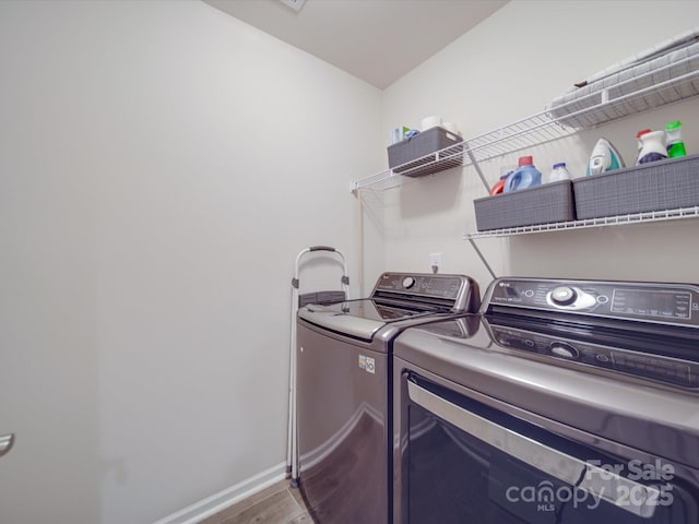 washroom featuring laundry area, baseboards, wood finished floors, and washing machine and clothes dryer