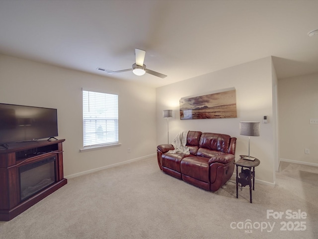 living area with carpet floors, a ceiling fan, baseboards, and a glass covered fireplace