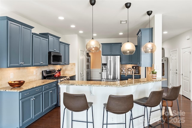 kitchen with blue cabinetry, a kitchen bar, appliances with stainless steel finishes, a peninsula, and dark wood-style floors