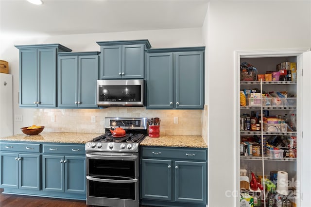 kitchen with appliances with stainless steel finishes, tasteful backsplash, blue cabinets, and light stone counters