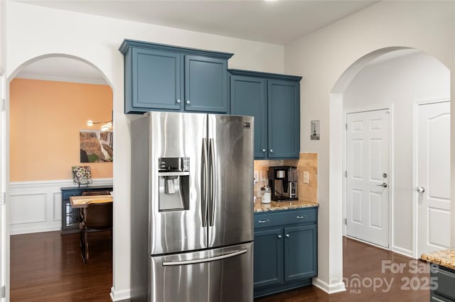 kitchen featuring dark wood-style flooring, light stone countertops, stainless steel fridge, blue cabinets, and arched walkways